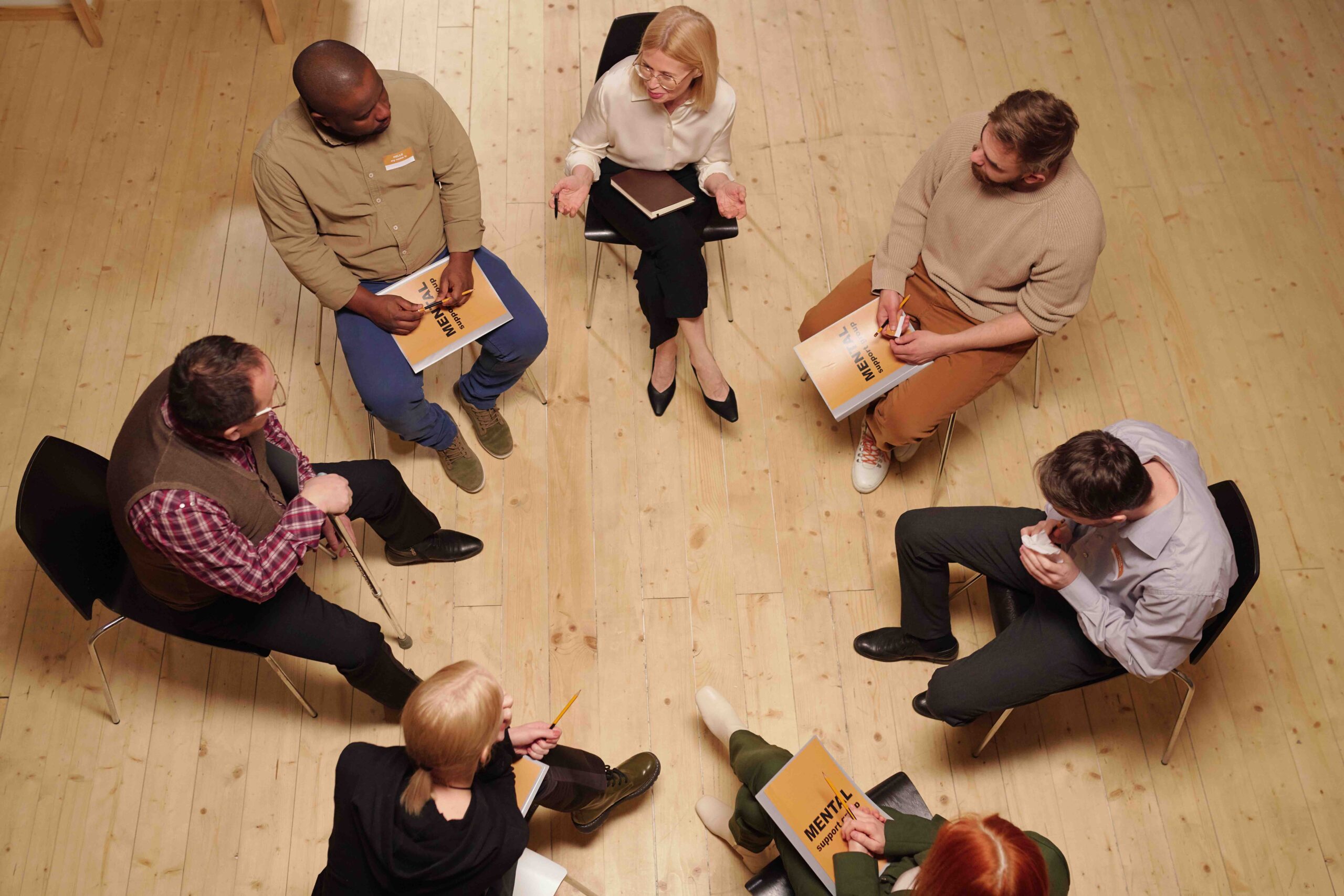 Above view of several patients talking to psychologist while sitting on chairs in circle