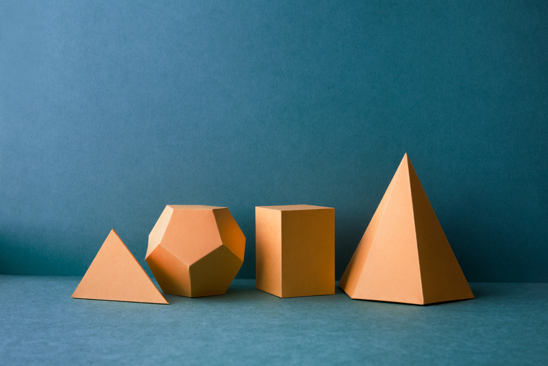 Abstract geometric figures. Three-dimensional dodecahedron pyramid tetrahedron cube rectangular objects on blue background. Yellow color Platonic solids still life background